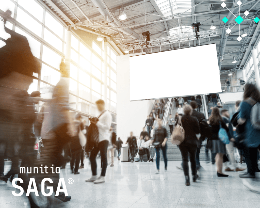Crowds of people moving through a modern airport terminal with a large digital screen above, symbolizing the scale and complexity of online activity that phishing domain detection with AI helps monitor and secure in real time.