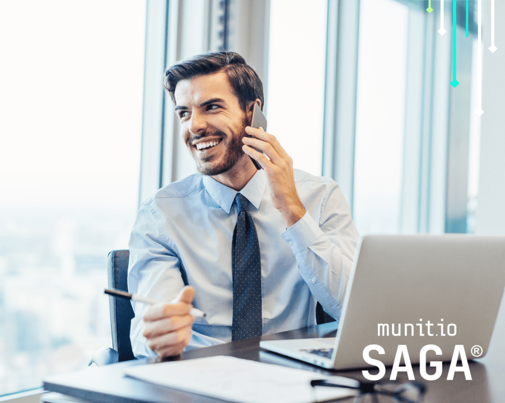 A business professional speaking on a smartphone while working on a laptop, illustrating social engineering scenarios relevant to what is SIM swapping and account takeover risks.