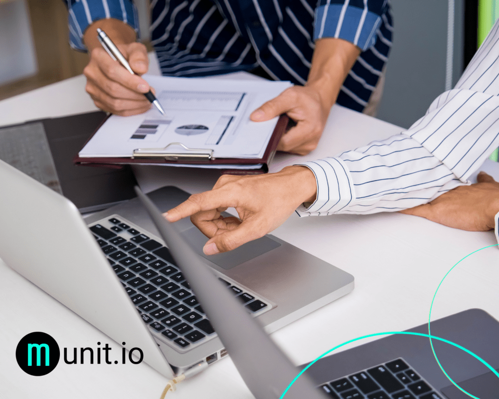 Two professionals reviewing printed charts while pointing at a laptop screen during a security analysis session, reflecting How do you detect stolen employee credentials? through collaborative investigation and access monitoring.